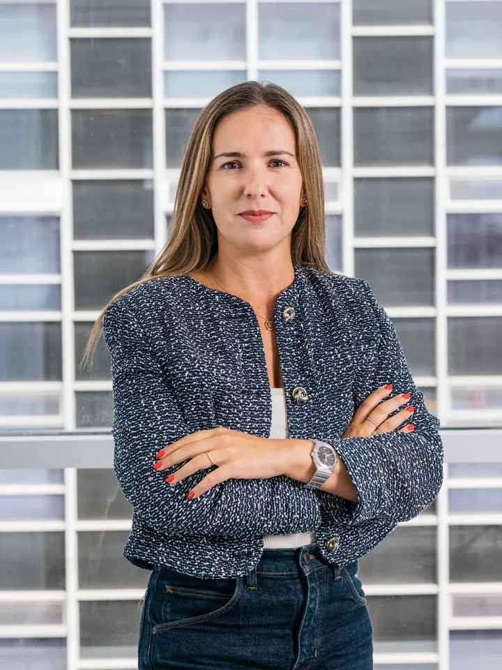 Rita Bastos, de HeliOx, con chaqueta de tweed azul y los brazos cruzados delante de un ventanal