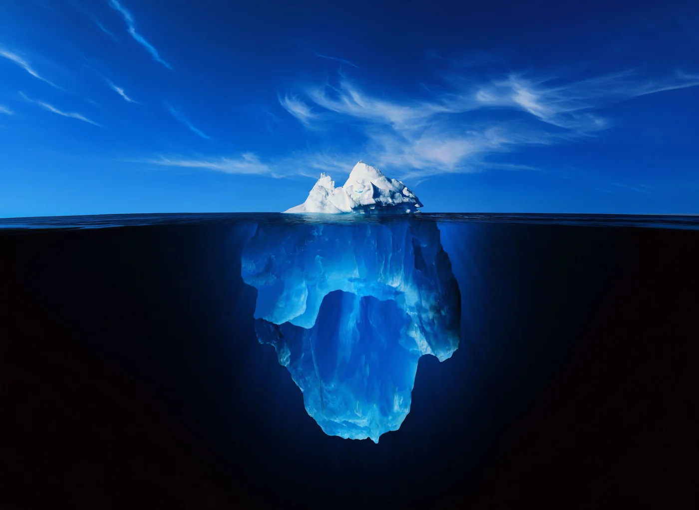 Un iceberg irregular asoma sobre el agua: la punta, iluminada bajo un cielo azul, es mucho menor que la masa azul que queda sumergida
