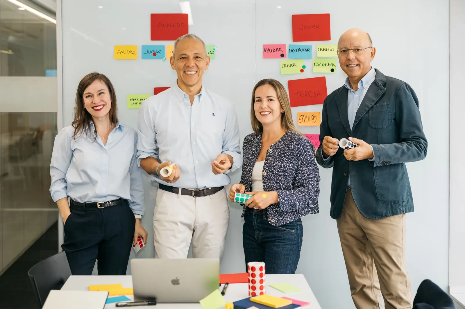 Las cuatro personas del equipo de HeliOx, de pie ante una pared de notas adhesivas, sujetan rollos de pegatinas y material de trabajo